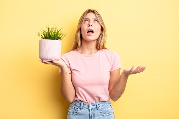 Pretty blonde girl looking desperate, frustrated and stressed. houseplant concept