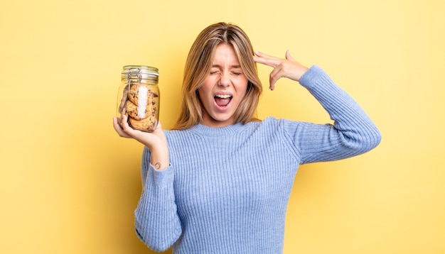 Pretty blonde girl looking unhappy and stressed, suicide gesture making gun sign. homemade cookies concept