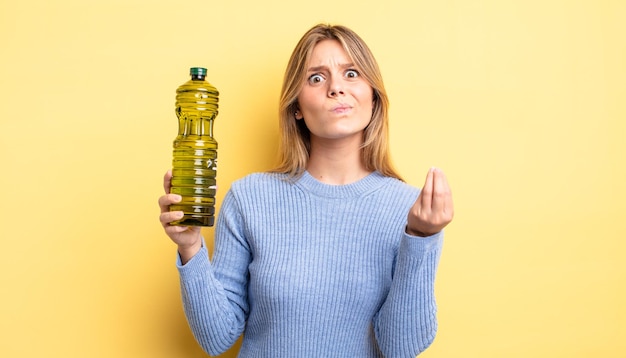 Pretty blonde girl making capice or money gesture, telling you to pay. olive oil concept