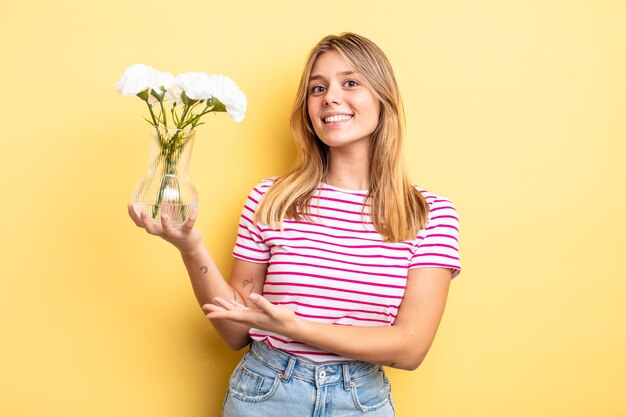 pretty blonde girl smiling cheerfully, feeling happy and showing a concept. decorative flowers concept