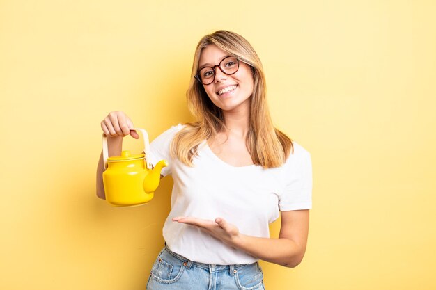 Pretty blonde girl smiling cheerfully, feeling happy and showing a concept. teapot concept