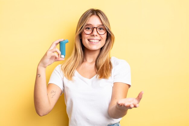 Ragazza bionda graziosa che sorride felicemente con amichevole e che offre e che mostra un concetto. concetto di inalatore per l'asma