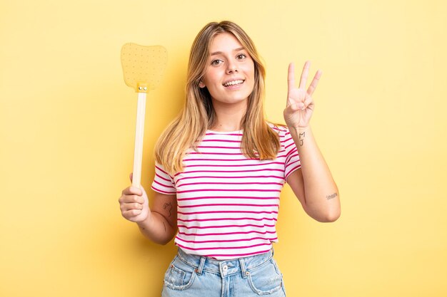 Pretty blonde girl smiling and looking friendly, showing number three. kill flies concept