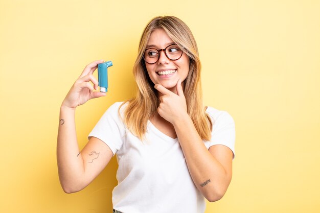 Pretty blonde girl smiling with a happy, confident expression with hand on chin. asthma inhaler concept