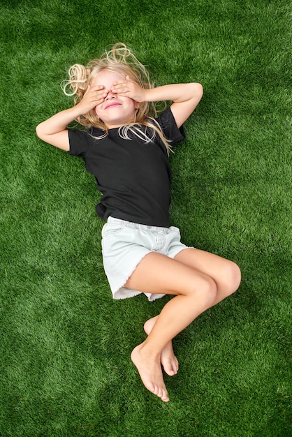 Photo pretty blonde girl with closed eyes lying stretching on green grass mock up black tshirt top view