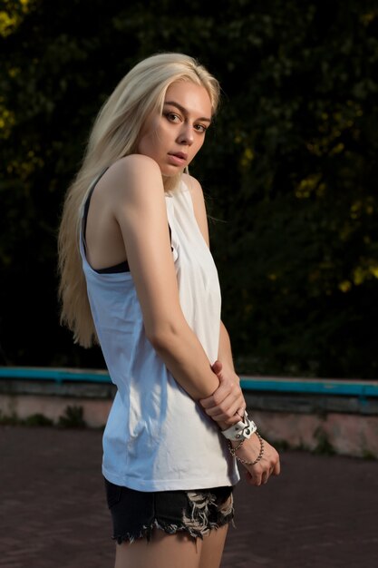 Pretty blonde girl with long hair dressed in fashionable clothes and posing in the park