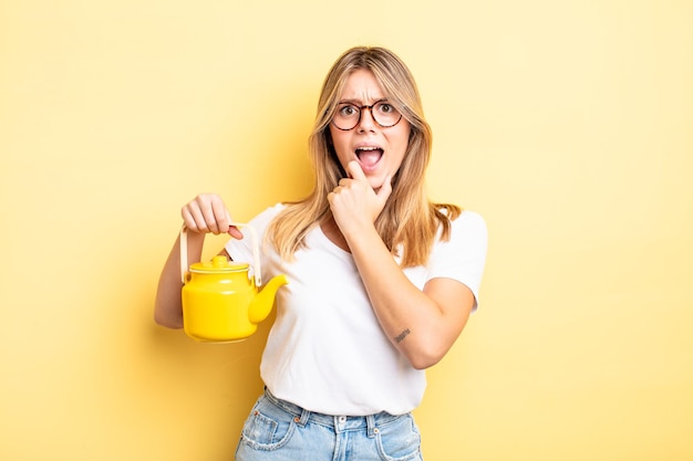 Pretty blonde girl with mouth and eyes wide open and hand on chin. teapot concept