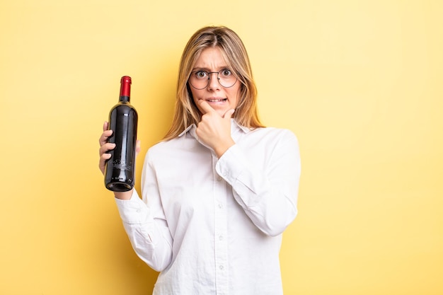 Pretty blonde girl with mouth and eyes wide open and hand on chin. wine bottle concept