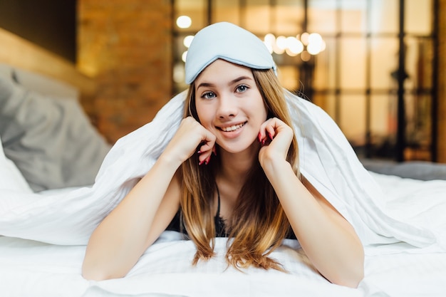 Pretty blonde in her bed in blue pajamas and sleep mask.