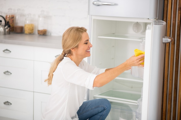 사진 냉장고를 청소하고 웃고 흰 셔츠에 예쁜 금발 주부