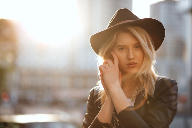 Pretty blonde lady wearing black hat posing with warm sun light. Space for text