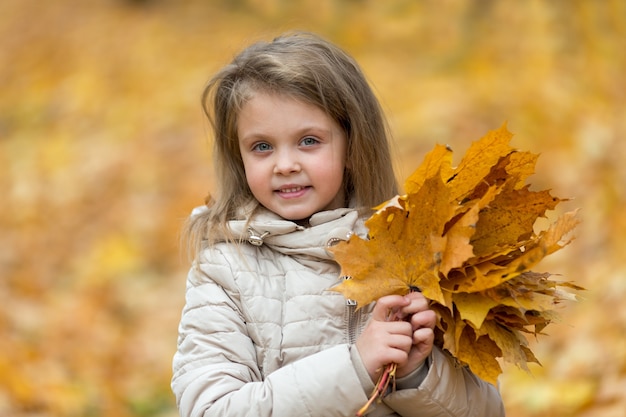 紅葉を保持している秋の森のかわいい金髪の少女