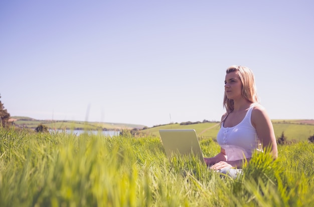 Pretty blonde sitting on grass using her laptop