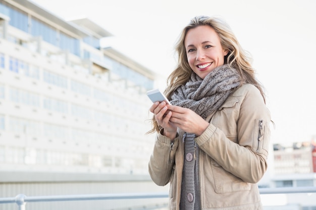 Piuttosto bionda in piedi e utilizzando smartphone