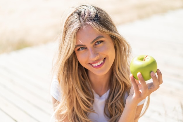 Photo pretty blonde uruguayan woman with an apple and happy