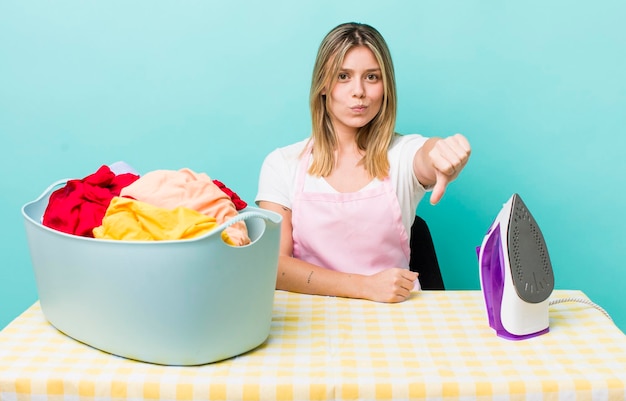 Pretty blonde woman feeling crossshowing thumbs down iron and clothes concept