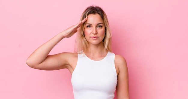 Pretty blonde woman greeting the camera with a military salute in an act of honor and patriotism showing respect