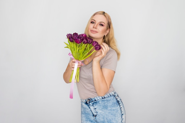 Pretty blonde woman holding purple tulips in her hands 