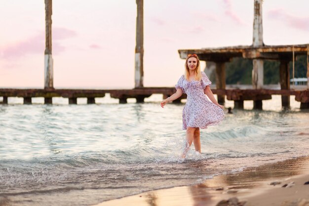 写真 美しい金の女性がビーチを歩いています地平線と夕暮れのピンクの空が背景です夏休みの自由と心理学の概念です