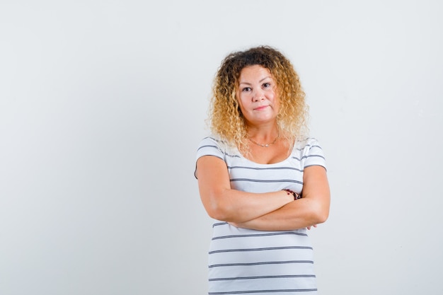 Foto bella donna bionda che tiene le braccia conserte in una t-shirt a righe e sembra sensata, vista frontale.