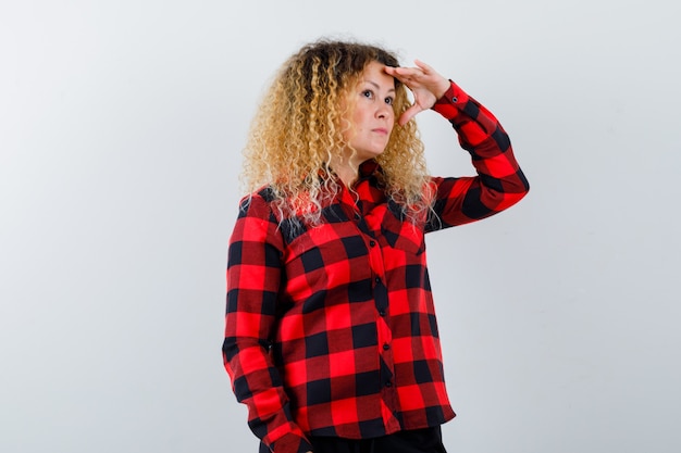 Pretty blonde woman looking far away with hand over head in checked shirt and looking pensive. front view.