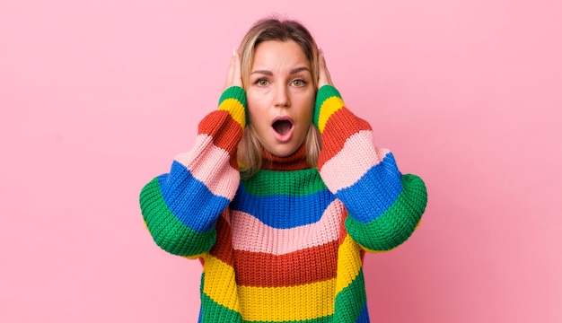 Pretty blonde woman looking unpleasantly shocked scared or worried mouth wide open and covering both ears with hands