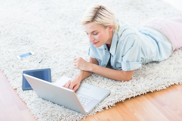 Pretty blonde woman lying on the floor and using her laptop