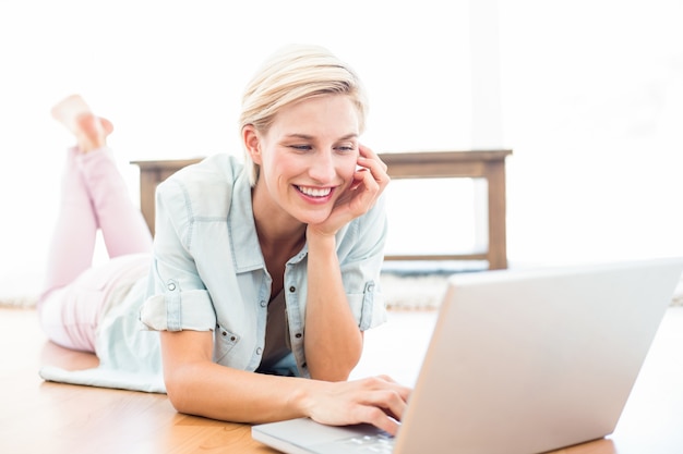 Photo pretty blonde woman lying on the floor and using her laptop