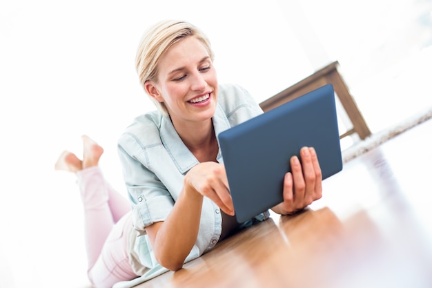 Pretty blonde woman lying on the floor and using her tablet