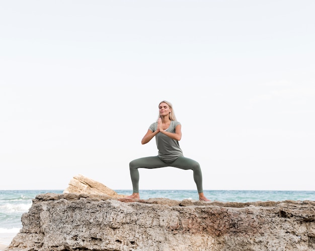 Pretty blonde woman practicing yoga at the beach