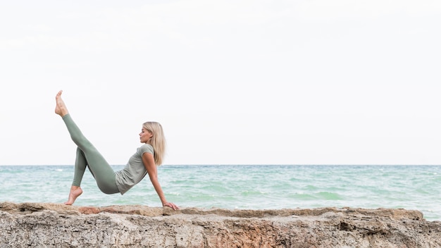 Pretty blonde woman practicing yoga at the beach