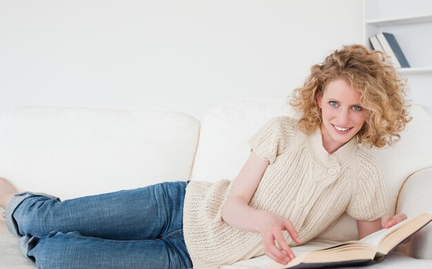 Довольно блондинка женщина, чтение книги, лежа на диване