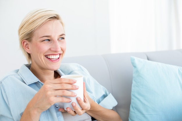 Pretty blonde woman relaxing on the couch and holding a mug