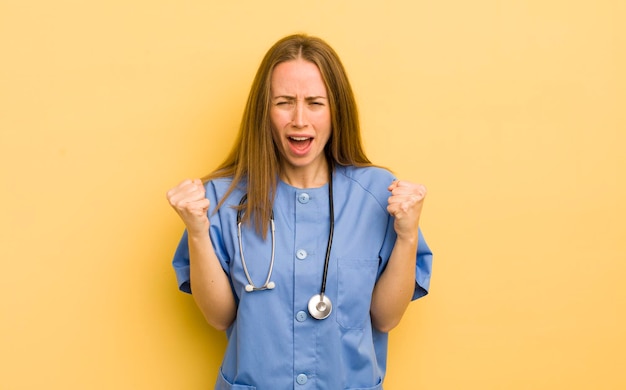 Pretty blonde woman shouting aggressively with an angry expression nurse concept