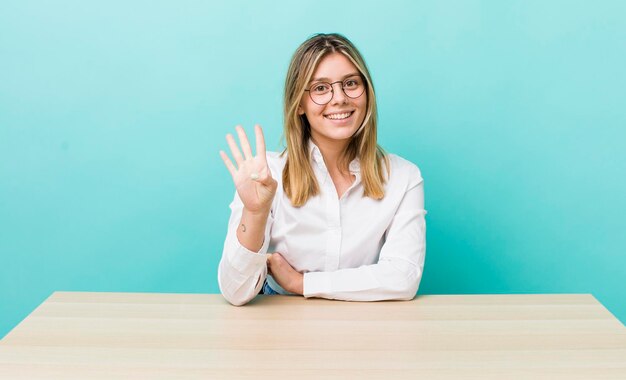 Pretty blonde woman smiling and looking friendly showing number four business and desk concept