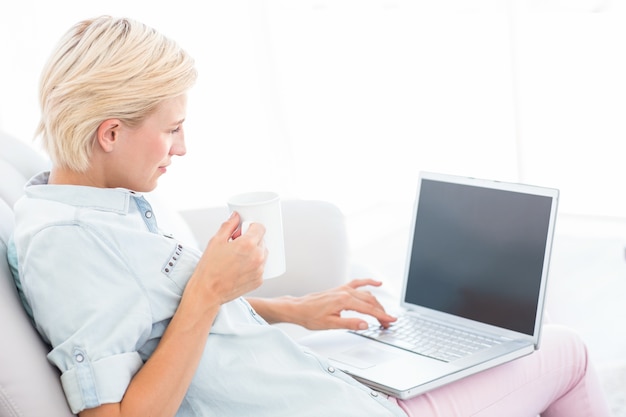 Pretty blonde woman using her laptop and holding mug