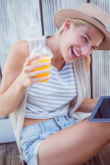 Photo pretty blonde woman using her tablet and holding orange juice