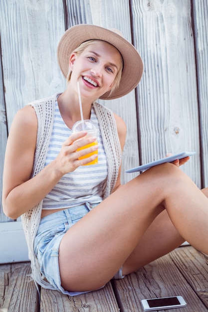 Pretty blonde woman using her tablet and holding orange juice