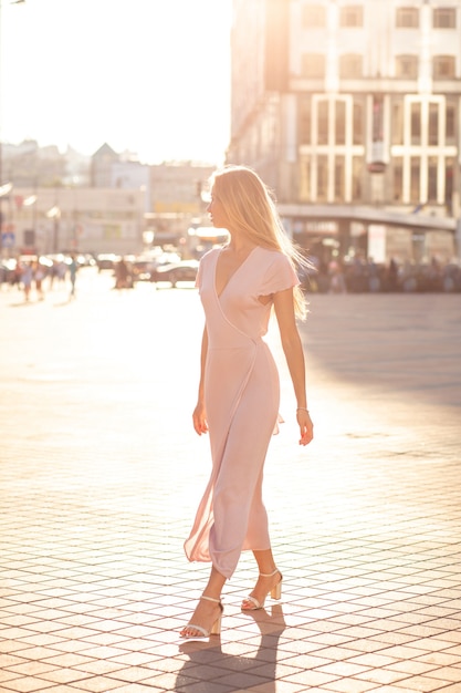 Pretty blonde woman with fluttering hair wearing long knitted dress walking down the street