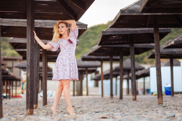 Foto una bella giovane donna bionda in abito che posa vicino agli ombrelli da spiaggia il concetto di libertà e psicologia delle vacanze estive