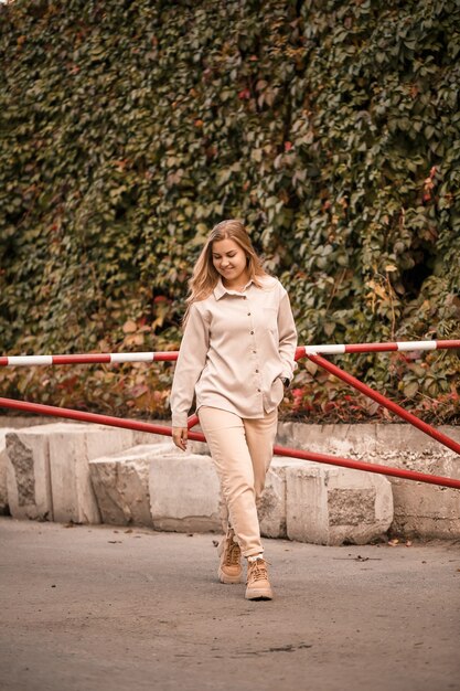 A pretty blonde young woman is walking down the street, she is wearing jeans and a beige shirt. Beautiful girl dressed in casual style with a smile on her face for a walk