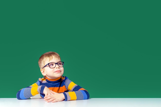 A pretty boy in glasses is sitting at the table looking away Copy space