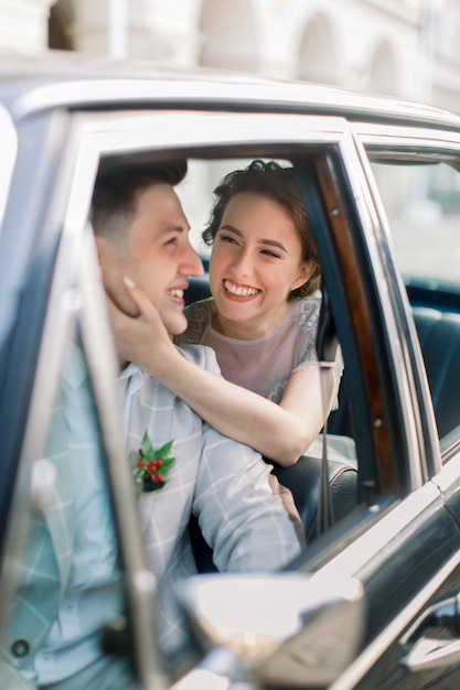 Pretty bride and handsome groom in the retro car in old city center