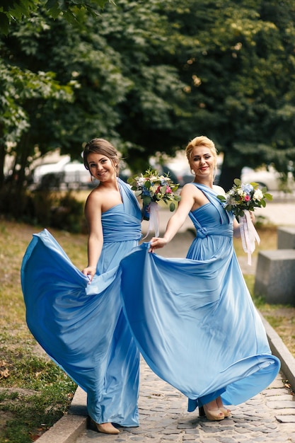 Pretty bridesmaids whirl their blue gowns standing on path in park