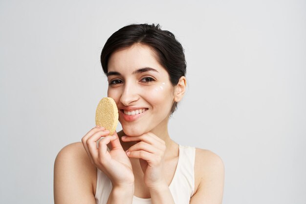 Pretty brunette clean face skin sponge in hands with cosmetics person