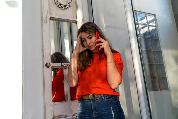 写真 赤いtシャツを着た美しい茶色の女性デザイナーが職場で電話で話しています