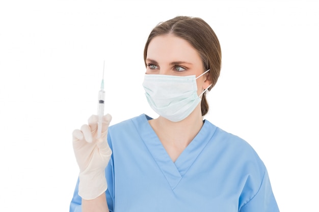 Pretty brunette female doctor holding a syringe and looking at it