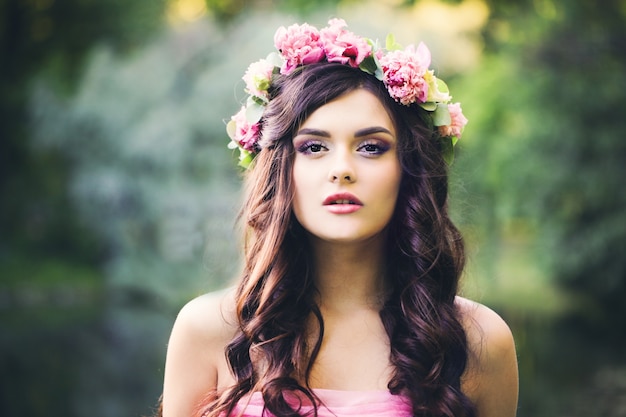 Pretty Brunette Girl with Curly Hairstyle Outdoors. Fashion Woman in Park. Makeup, Dark Wave Hair, Flowers