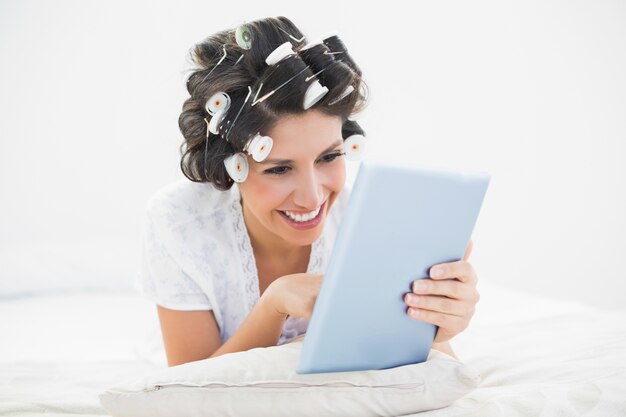 그녀의 태블릿을 사용하여 그녀의 침대에 누워 머리 롤러에 예쁜 갈색 머리