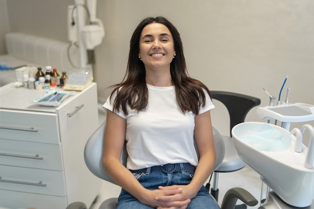 Pretty brunette happy female patient sitting in the chair at dental clinic.